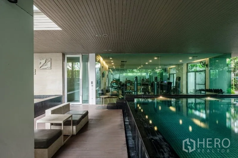 Condominium for sale - Poolside lounge seating beside indoor swimming pool and glass-walled gym.