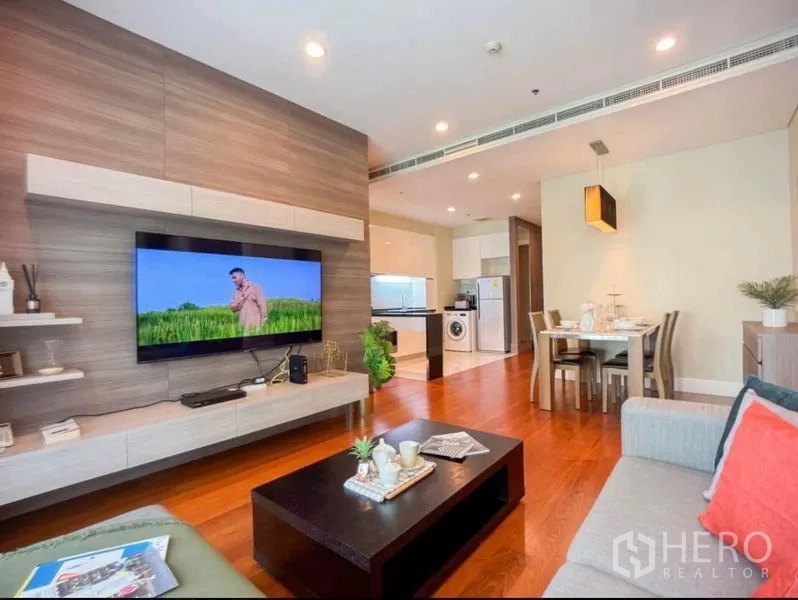 Condominium for rent in Khlong Toei, Bangkok - Open-plan living room with wood floors, a floating TV wall, dining area and modern kitchen in a Bangkok condo.