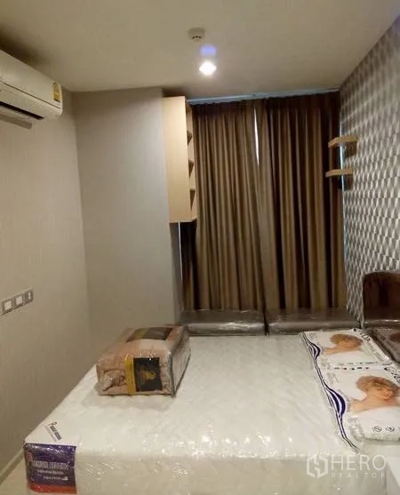 Condominium for rent in Khlong Toei, Bangkok - Furnished bedroom featuring a large bed, padded feature wall, blackout curtains and wall-mounted air conditioner.