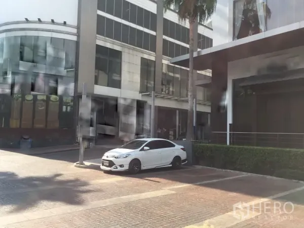 Retail Space for rent in Khlong Toei, Bangkok - Modern commercial complex with parking, palm trees and a glass façade near a transit hub.
