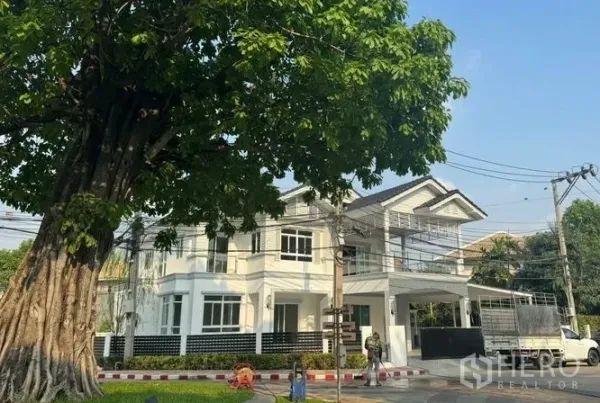 独立式住宅 出售在Pak Kret, Nonthaburi - 大树遮荫的正立面，带阳台、大门和有顶停车位
