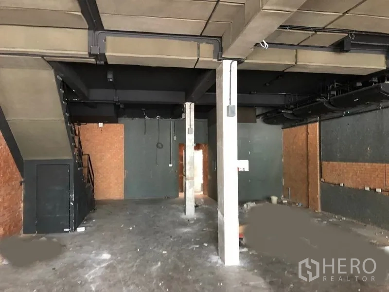 店屋 出租在Watthana, Bangkok - 一层室内挑高空间，外露管线与混凝土立柱，带内部楼梯。