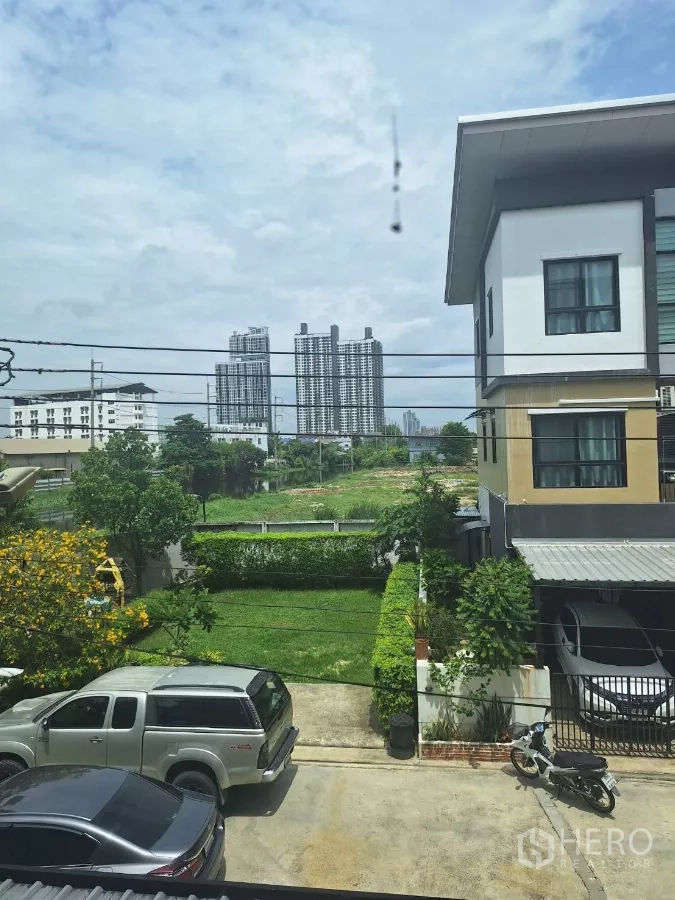 Townhouse for rent in Mueang Samut Prakan, Samut Prakan - Upper-floor view of a townhouse garden and driveway with distant city high-rises.