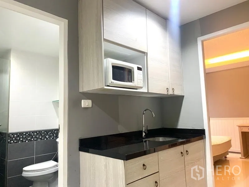 Condominium for rent in Khlong Toei, Bangkok - Pantry with sink, upper cabinets and microwave beside doorway to bathroom and bedroom.
