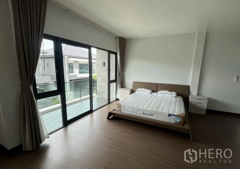 Detached House for rent in Bang Phli, Samut Prakan - Bedroom opening to a balcony through large sliding doors and warm wood flooring.