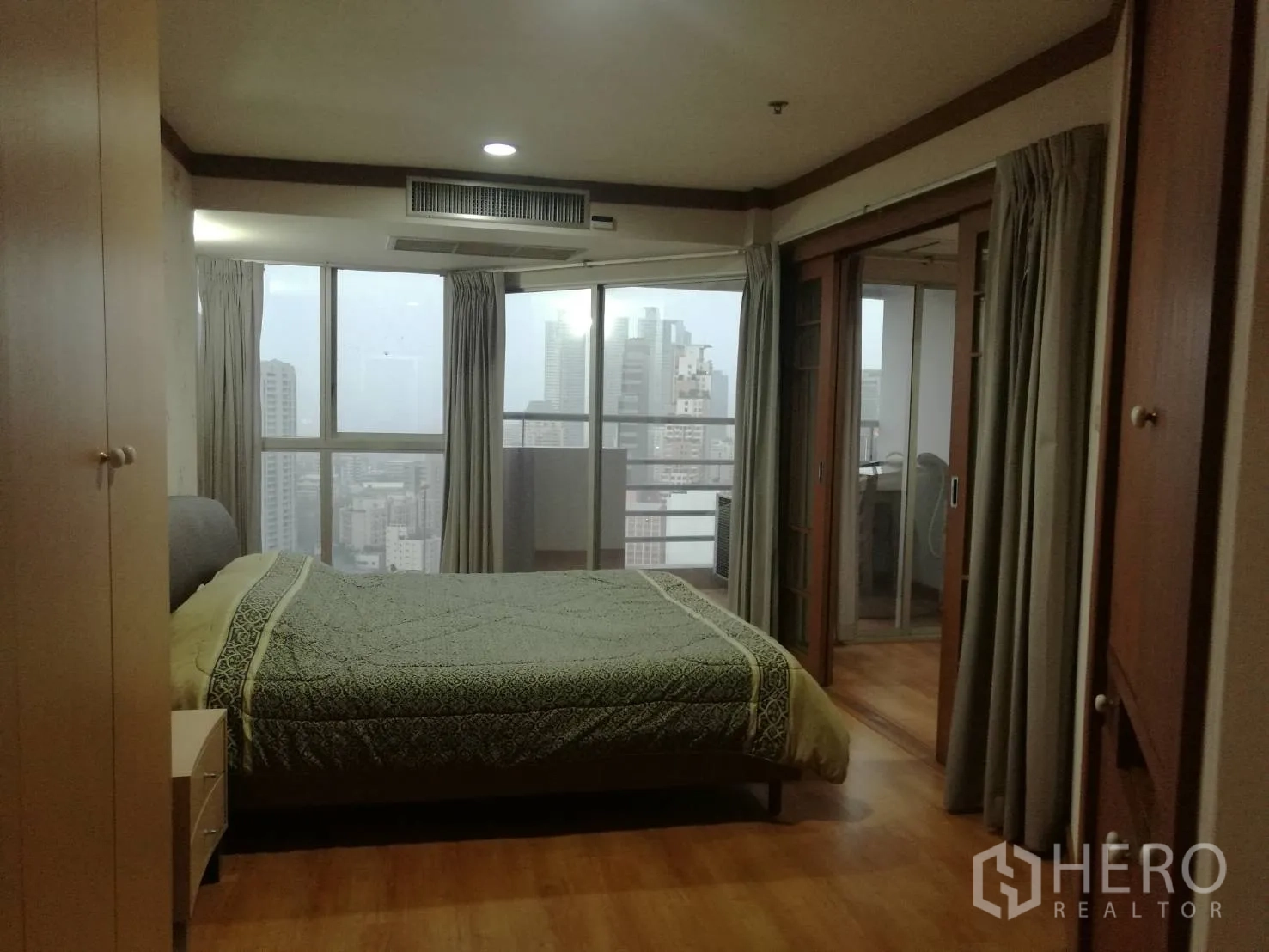 Condominium for rent in Khlong Toei, Bangkok - Bedroom with large windows, city skyline view and sliding doors to the balcony.
