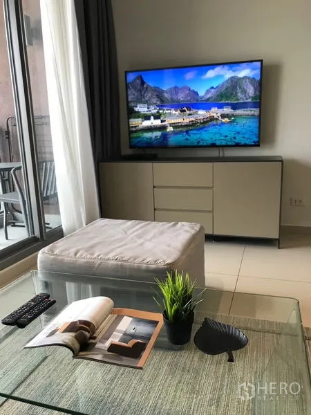 公寓 出租在Watthana, Bangkok - 瓦他那区公寓的电视角与阳台，茶几上有绿植和杂志