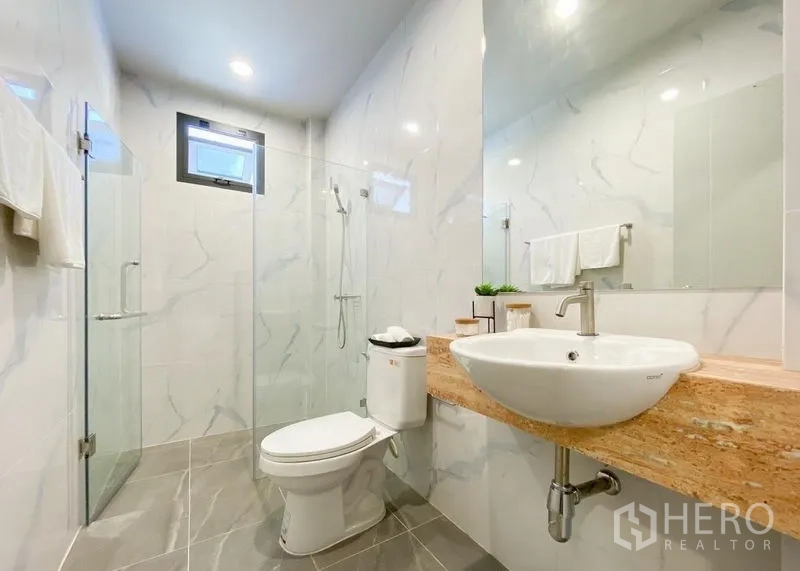 Detached House for sale in Lam Luk Ka, Pathum Thani - Modern bathroom with glass shower enclosure and wide mirror.