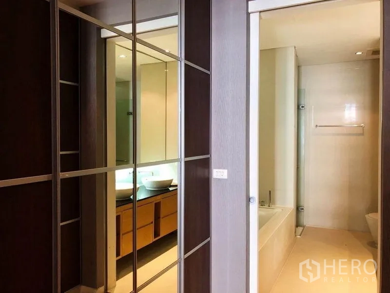 Condominium for rent in Khlong Toei, Bangkok - Bathroom entry with mirrored wardrobe, double vessel sinks and a bathtub with separate shower.