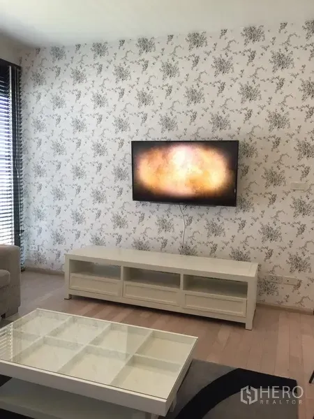 Condominium for rent in Watthana, Bangkok - Living area with wall-mounted TV, white media console and floral feature wall.