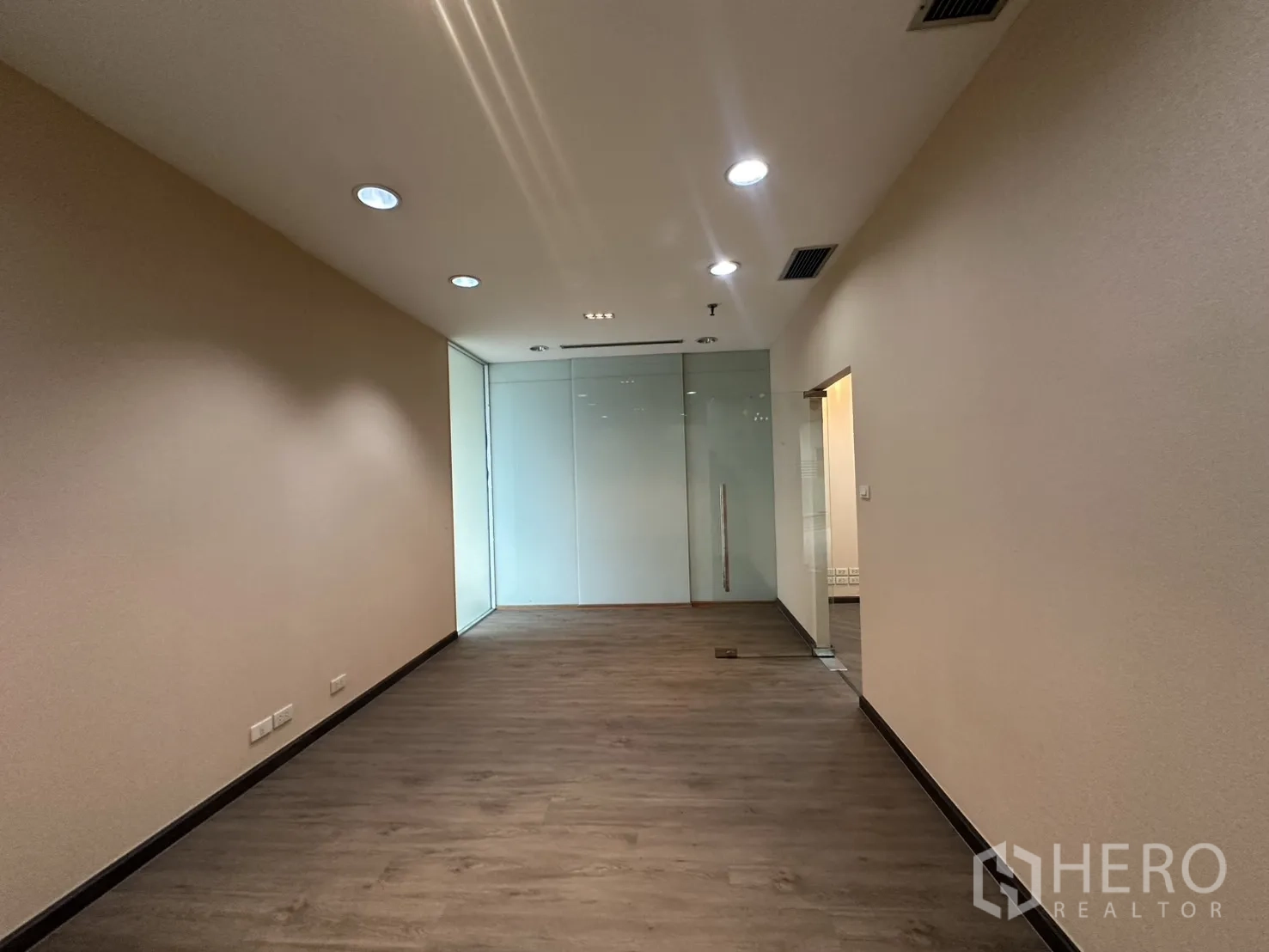 Office Space for rent in Bang Rak, Bangkok - Long workspace with a glass partition wall and ceiling spotlights.