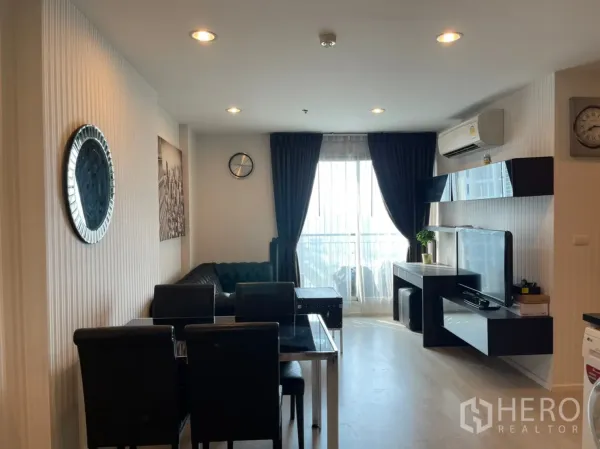 Condominium for sale in Sathon, Bangkok - Living room facing floor-to-ceiling window with TV console, shelving and blackout curtains.