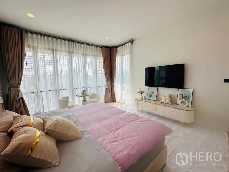 Detached House for rent or sale in Bang Kapi, Bangkok - Primary bedroom from alternate view with TV console and small round table and chairs by the windows.