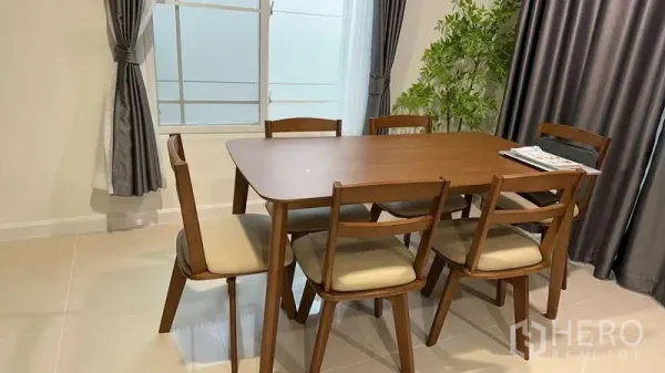 Detached House for rent in Bang Kapi, Bangkok - Wood dining table for six beside large windows and curtains.