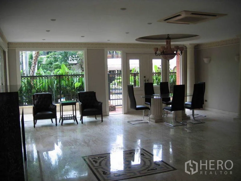 Detached House for rent in Watthana, Bangkok - Dining area with chandelier and glass doors opening to a garden patio with lush plants.