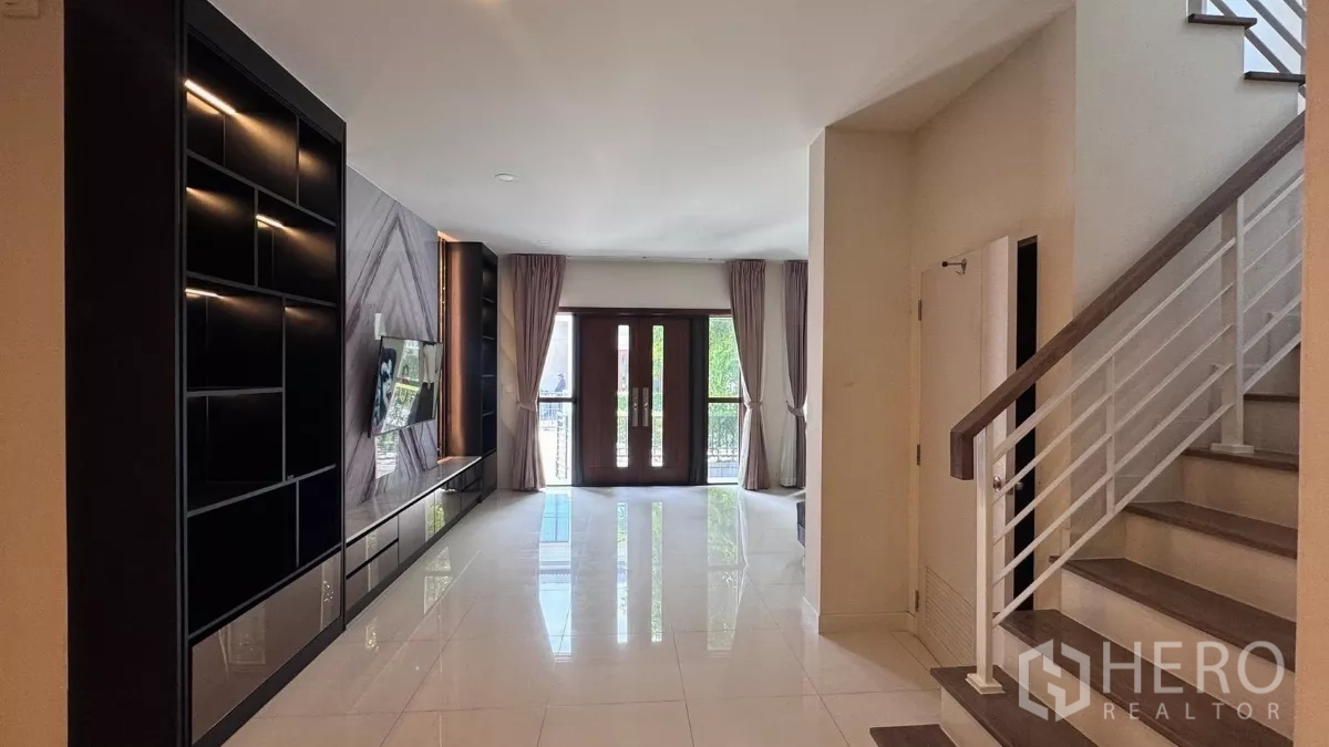 Detached House for rent or sale in Saphan Sung, Bangkok - Open‑plan lounge with glossy tile floors, long media cabinet and staircase with white railing leading upstairs.