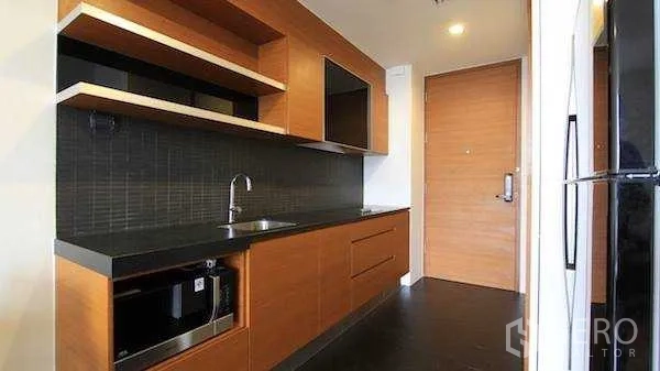 Condominium for rent - Modern galley kitchen with wooden cabinetry, black countertop and built‑in appliances.