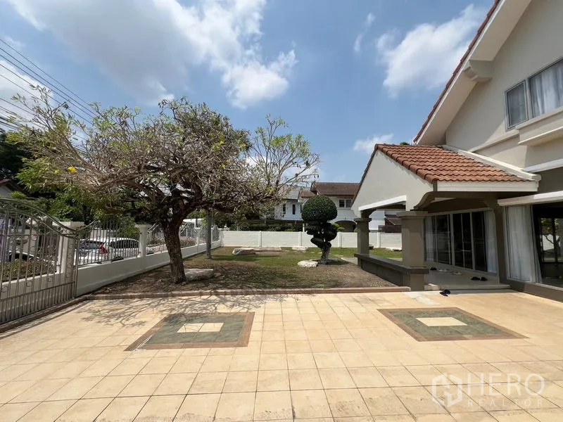 独立式住宅 出售在Mueang Pathum Thani, Pathum Thani - 独立屋前院铺砖庭院，成树与带顶门廊相连。