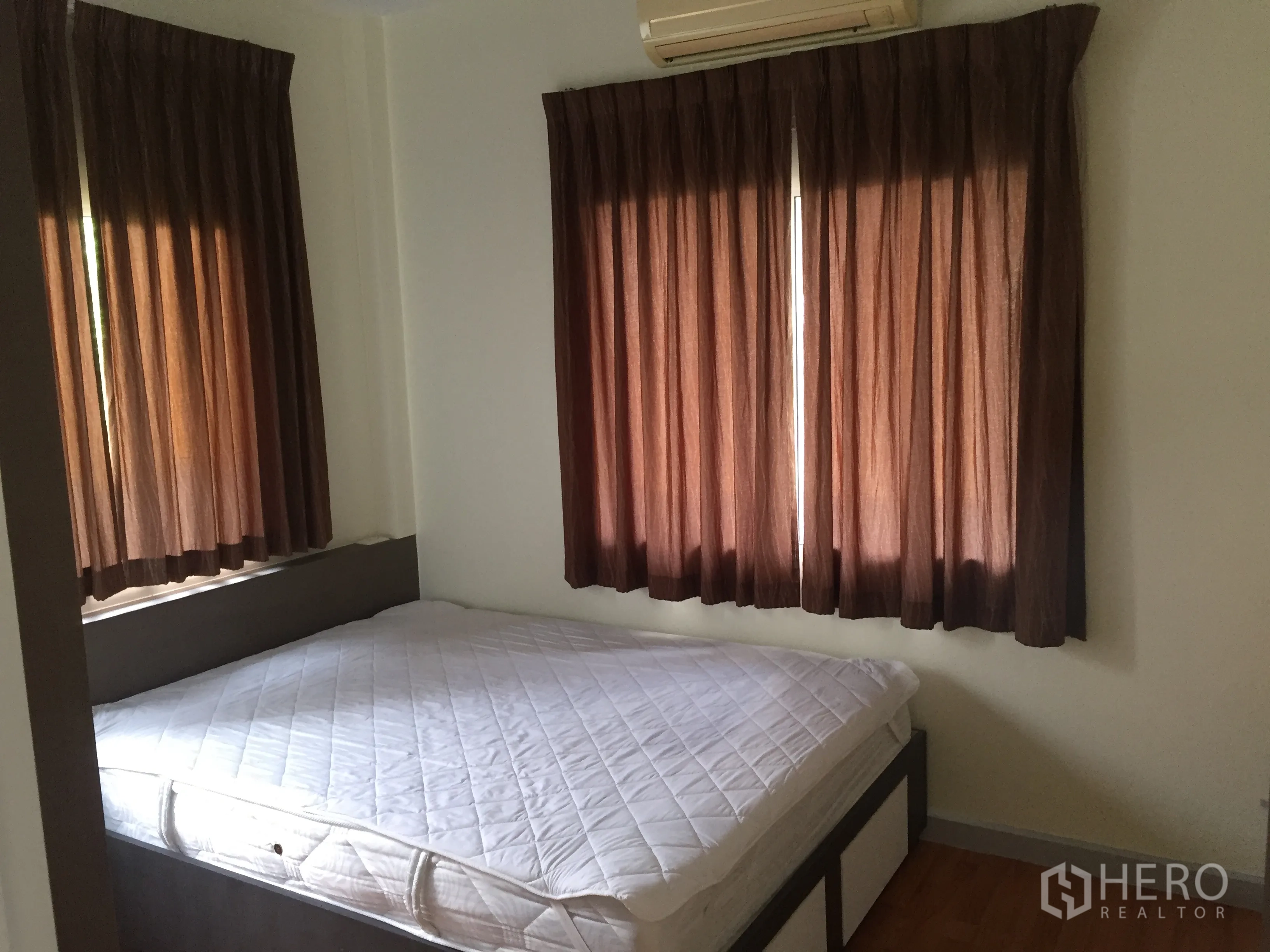 Detached House for sale in Lat Krabang, Bangkok - Cozy second bedroom with bed, brown curtains and air conditioner.