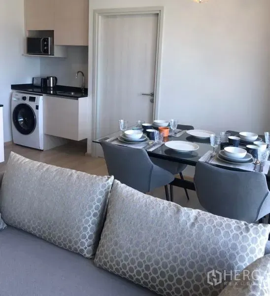 Condominium for rent in Huai Khwang, Bangkok - Compact kitchenette with microwave, sink and washing machine next to dining area.