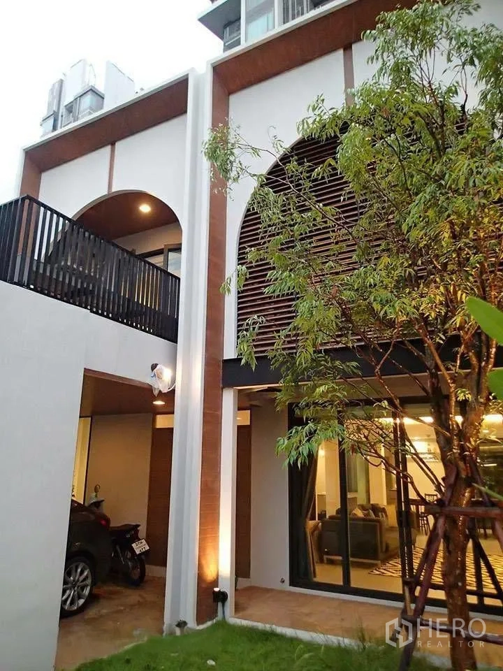 ทาวน์เฮาส์ for rent in Watthana, Bangkok - ด้านหน้าทาวน์เฮ้าส์สไตล์โมเดิร์น มีระเบียงโค้ง ไม้ระแนง โรงจอดรถ และสวนหญ้า