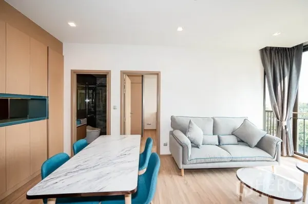 Condominium for rent in Watthana, Bangkok - Lounge with sofa and dining table beside full‑height corner windows.