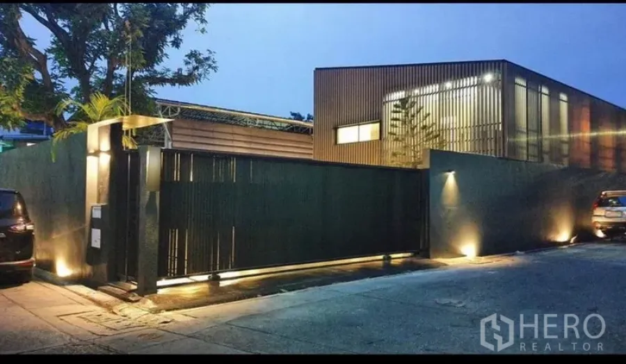 带办公室的家 出租或出售在Khlong Toei, Bangkok - 现代风格的带门禁家庭办公楼外观，高黑色围墙与暖光照明，位于Phra Khanong。
