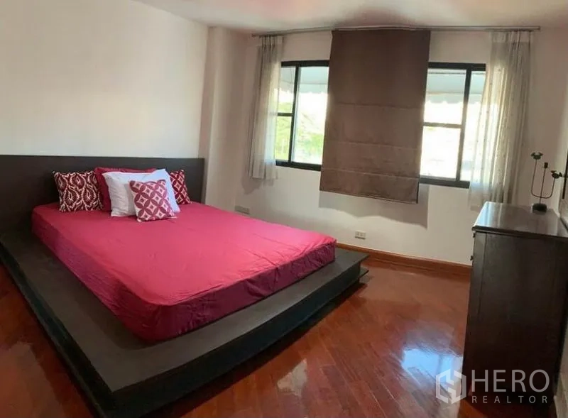 Townhouse for rent in Khlong Toei, Bangkok - Primary bedroom with platform bed, red bedding, hardwood floors and two windows.
