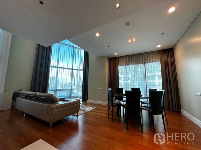 Condominium for rent in Khlong Toei, Bangkok - Open-plan living and dining room with floor-to-ceiling windows, city view and wood floors.