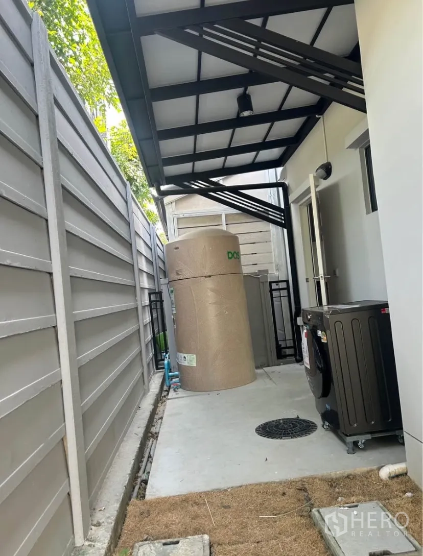 Semi-detached House for rent in Bang Phli, Samut Prakan - Covered side yard with utility area, water tank and washing machine beside a high privacy fence.