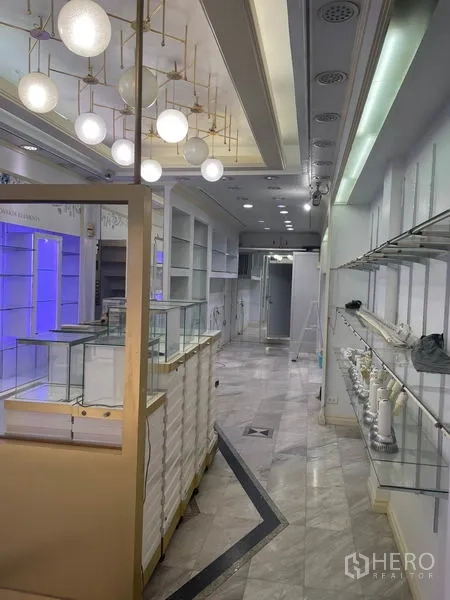 店屋 出租在Bang Rak, Bangkok - 过道设玻璃展示柜与发光展示架通向店铺后方。