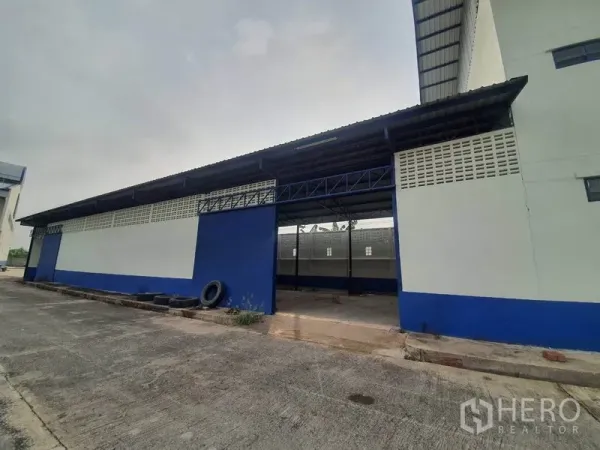 Factory for rent in Bang Bua Thong, Nonthaburi - Side view of a blue-and-white warehouse with a covered loading bay and large doorway.