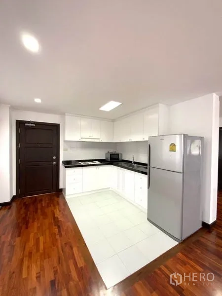 公寓 出租在Watthana, Bangkok - 紧凑白色厨房，黑色台面、吊柜、灶台与大冰箱，靠近入户门。