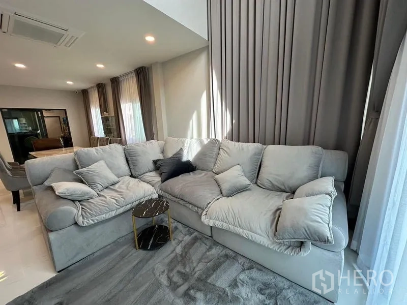 Detached House for rent in Bang Phli, Samut Prakan - Cozy corner with plush sectional sofa, floor-to-ceiling drapes and small side table on gray rug.