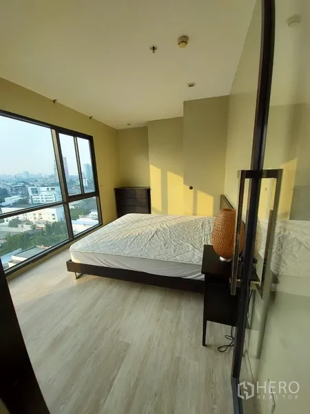 Condominium for rent in Phaya Thai, Bangkok - Corner bedroom with floor-to-ceiling windows and wide city views at sunset.