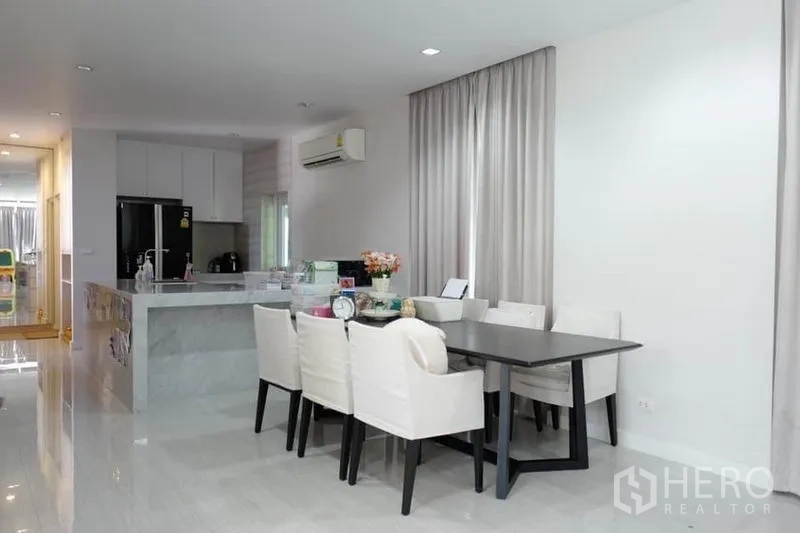 独立式住宅 出售在Pak Kret, Nonthaburi - 开放式餐厅，毗邻白色中岛厨房与高窗帘。