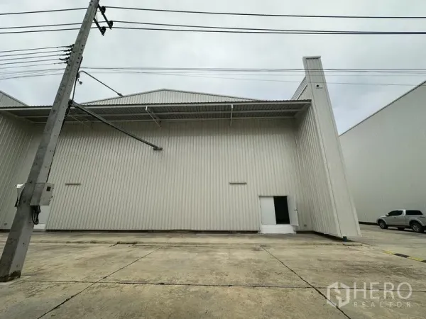 工厂 出租在Khlong Luang, Pathum Thani - 仓库侧立面，带雨棚、侧门和上方电力线。