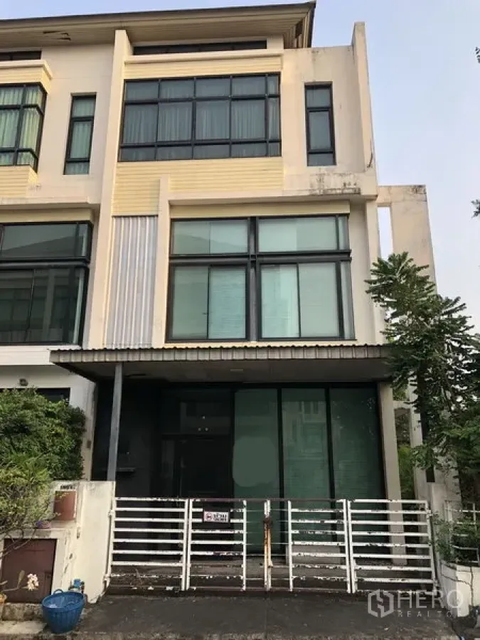 带办公室的家 出售在Wang Thonglang, Bangkok - 多层现代家庭办公楼外立面，整面落地窗与推拉门，入口带围栏，旁有绿植，位于曼谷旺通朗区。