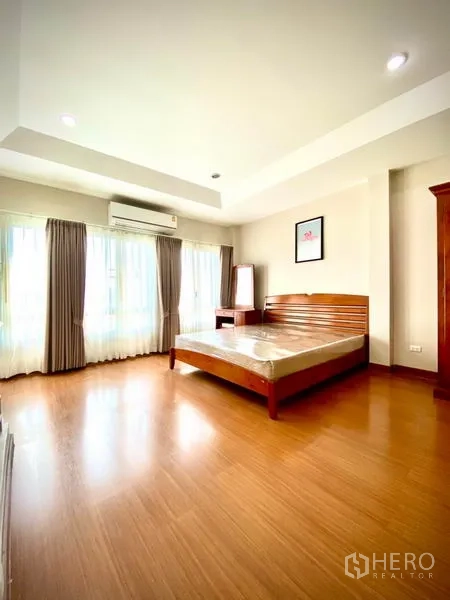 Townhouse for rent in Prawet, Bangkok - Master bedroom with tray ceiling, big windows, curtains, air conditioner and wooden bed.