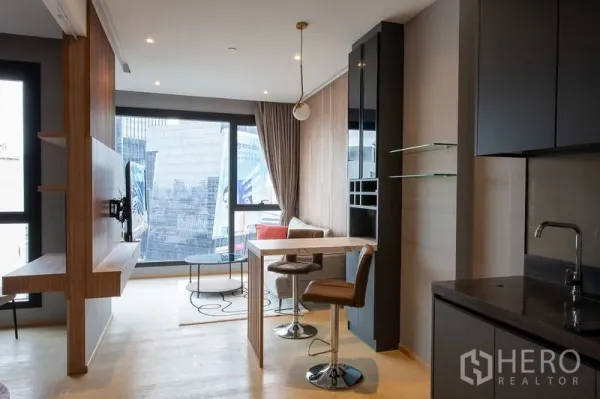 Condominium for rent in Din Daeng, Bangkok - Open-plan kitchen and living room with tall window, pendant light, bar dining set and skyline views in a modern Bangkok condo.