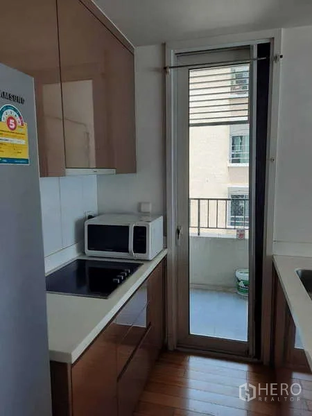 Condominium for rent in Khlong Toei, Bangkok - Kitchen with electric cooktop, microwave, and a door to the service balcony.