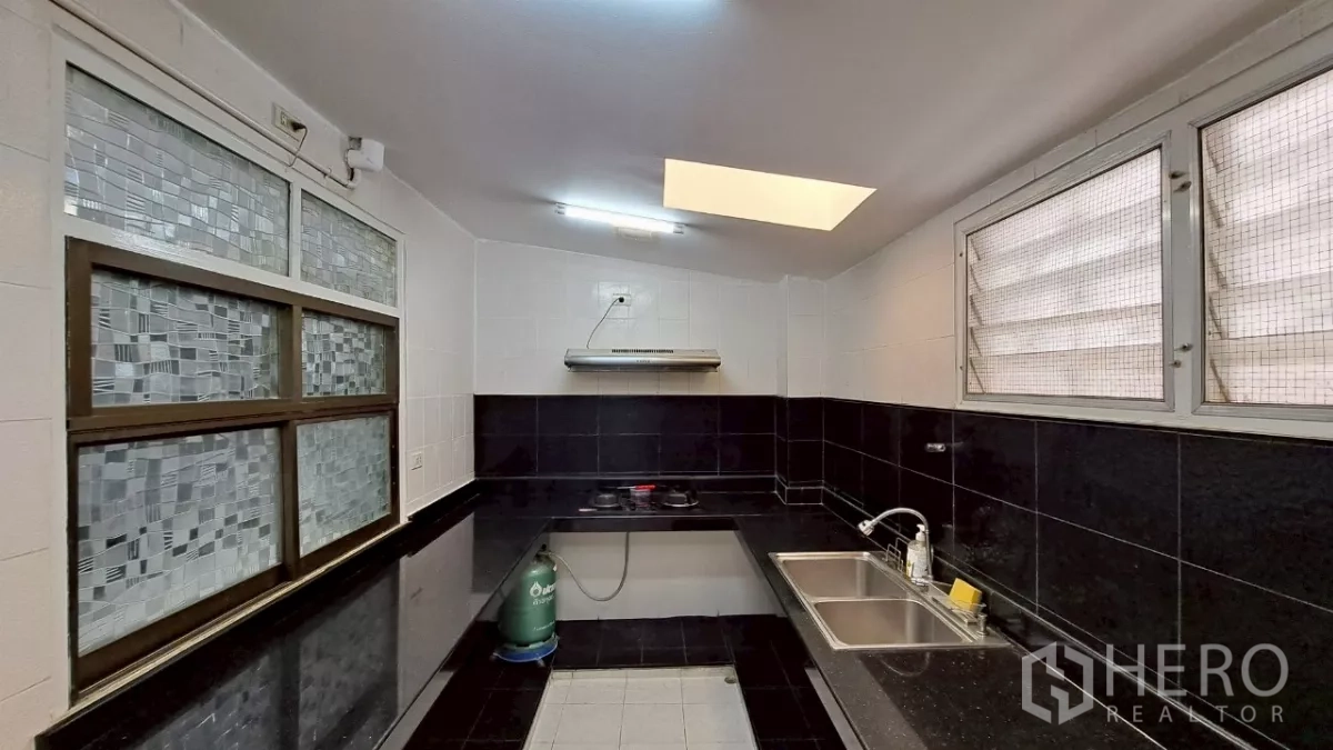 联排别墅 出租在Watthana, Bangkok - U 形泰式厨房，燃气灶，黑色墙砖与天窗。
