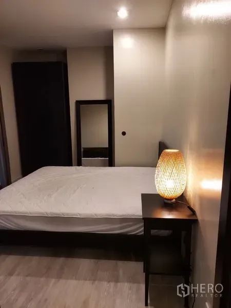 Condominium for rent in Phaya Thai, Bangkok - Cozy bedroom with bedside table and woven lamp, mirror and wood-look flooring.