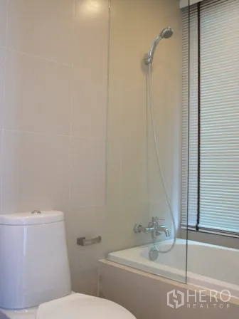 Condominium for rent in Watthana, Bangkok - Clean bathroom with bathtub, handheld shower, glass screen, and toilet.