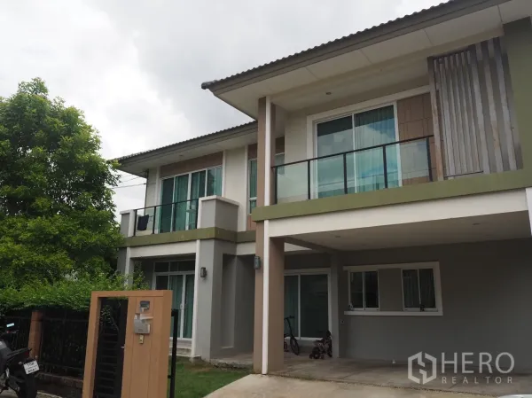 独立式住宅 出租在Pathum Thani - 两层独栋住宅外观，带阳台、遮雨车位、入户门与绿树环绕。