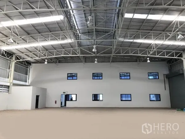 Factory for rent or sale in Bang Sao Thong, Samut Prakan - Warehouse interior facing the two-storey office block, high steel roof structure and a roller shutter door to the right.