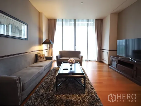 Condominium for rent in Sathon, Bangkok - Bright living room with sofa set, TV console and balcony-height windows.