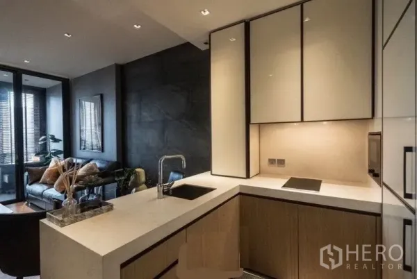 Condominium for rent in Khlong Toei, Bangkok - Sleek L-shaped kitchen with stone countertop, light cabinetry and open view to the living area.