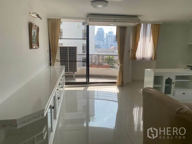 Condominium for rent in Watthana, Bangkok - Living area facing sliding glass doors to a balcony with skyline view and outdoor AC unit.