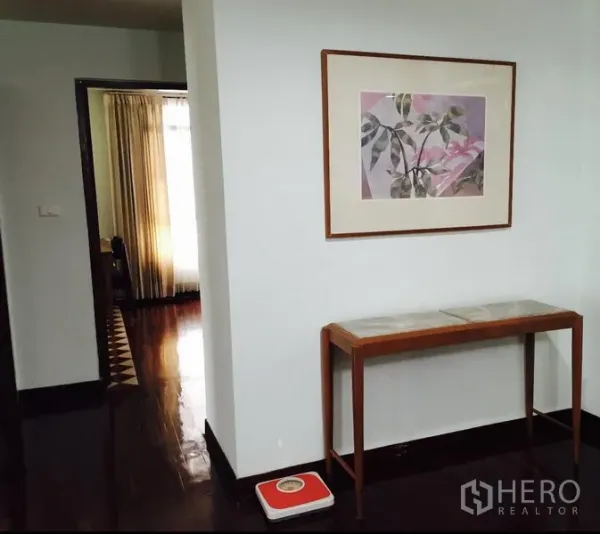 Condominium for rent in Watthana, Bangkok - Bright hallway with framed botanical artwork, slim console table and polished dark wood floors leading toward a room with curtains.